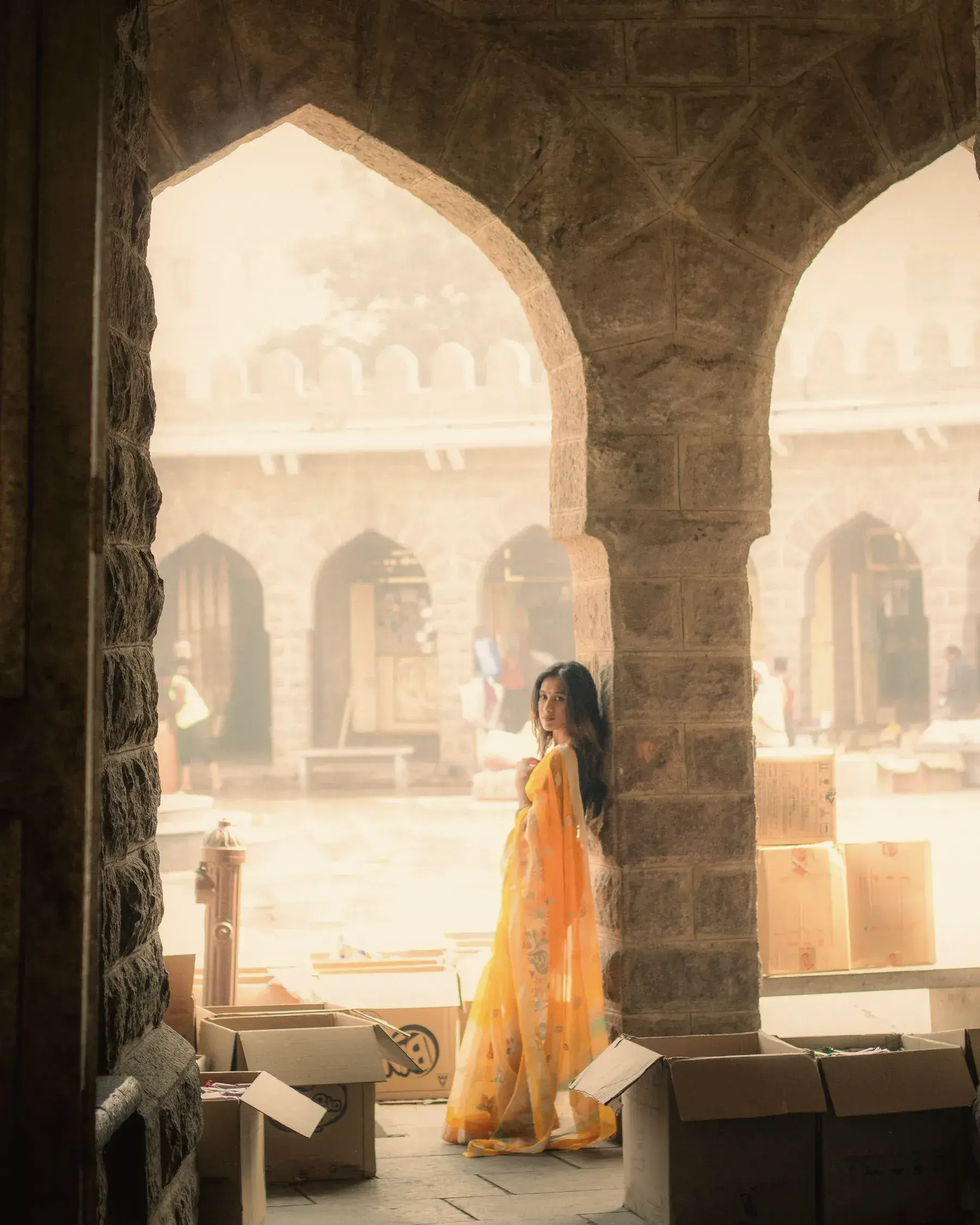 A woman in a yellow Chanderi saree standing under old stone arches
