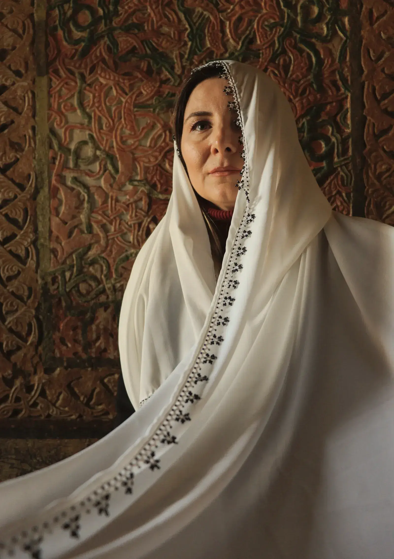 A woman wrapped in an ivory Dhakai jamdani, the border held across her body