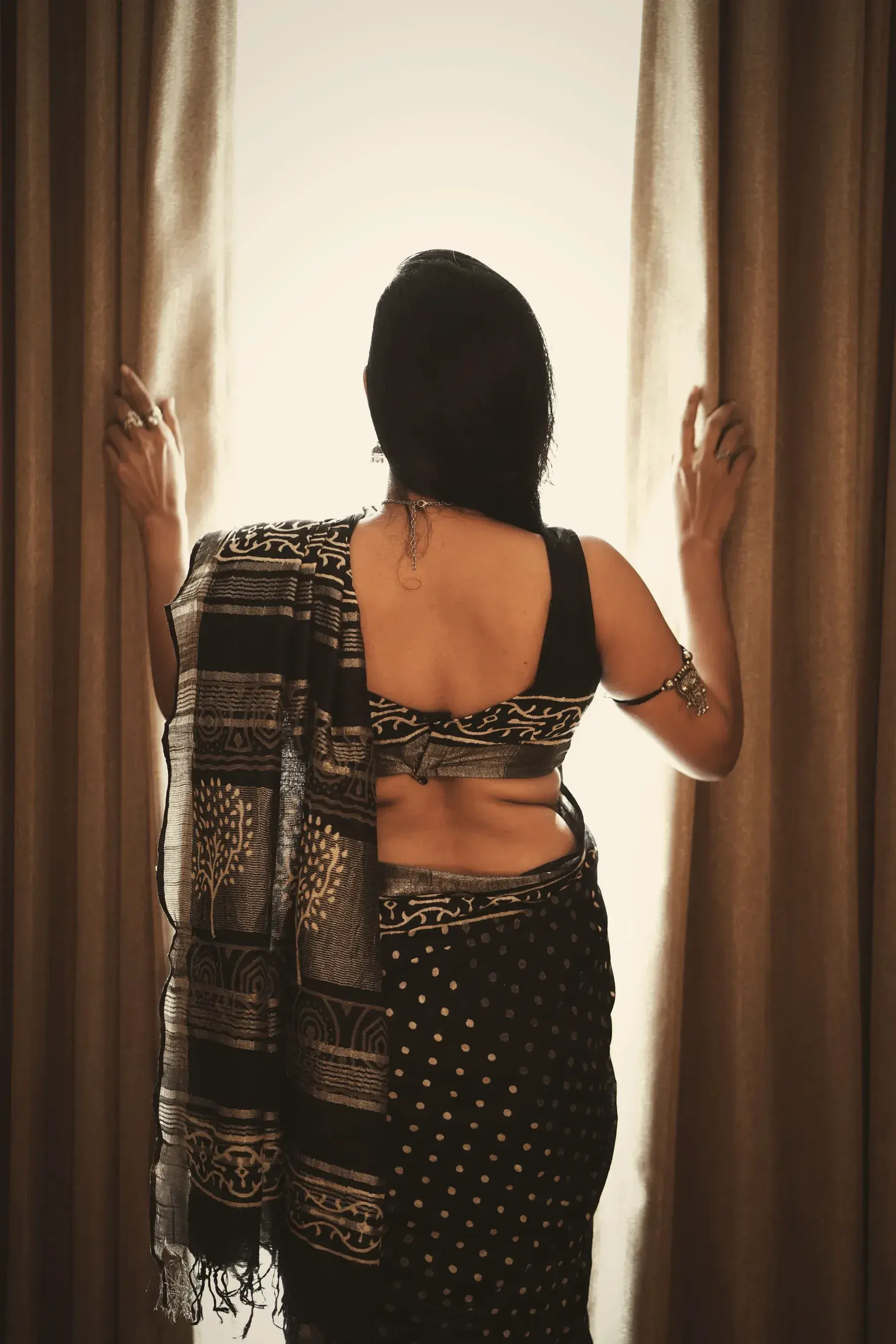 The black jamdani worn at a window with sheer curtains, seen from behind