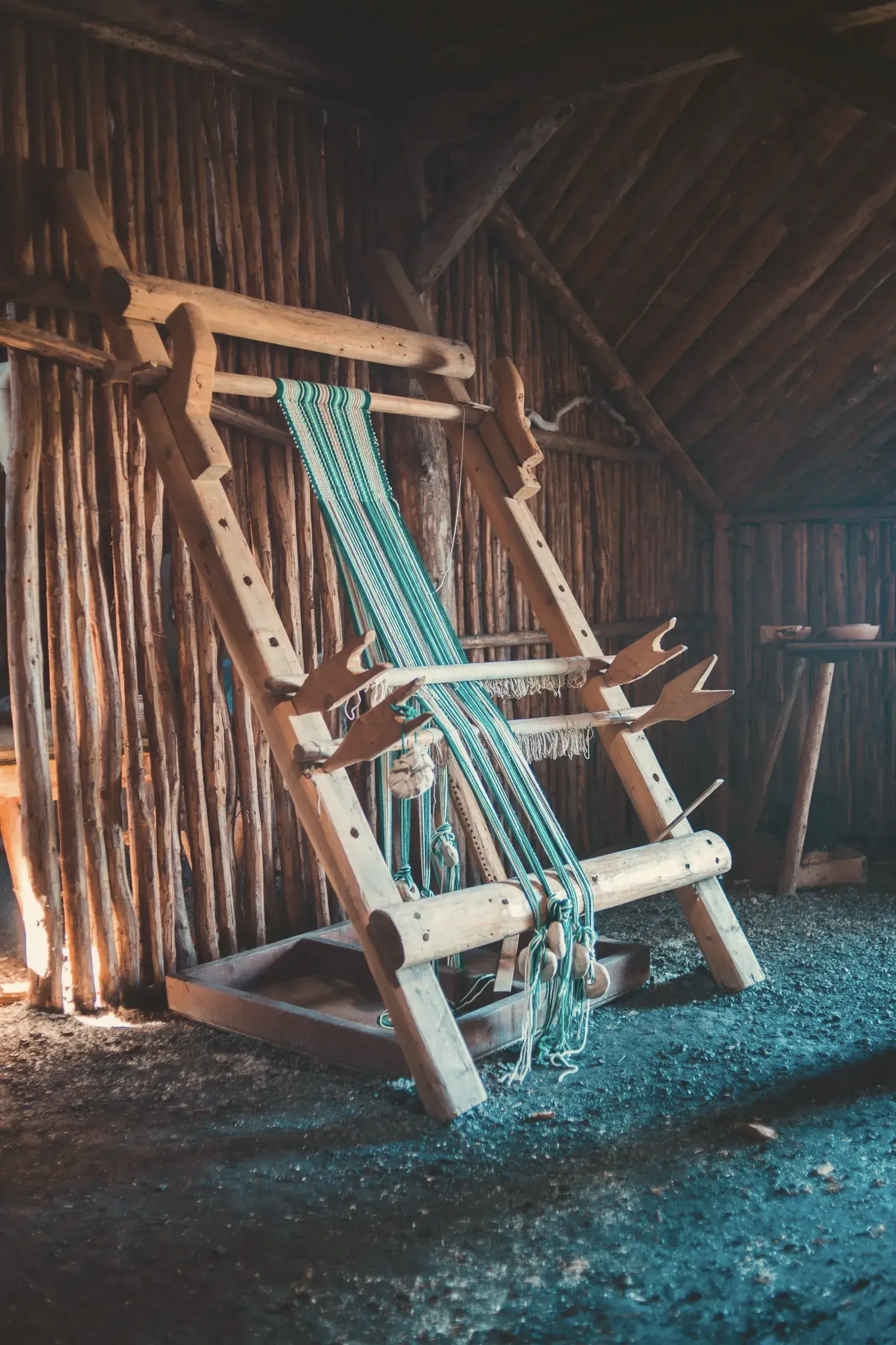 An old wooden loom strung with blue warp threads in a timber shed