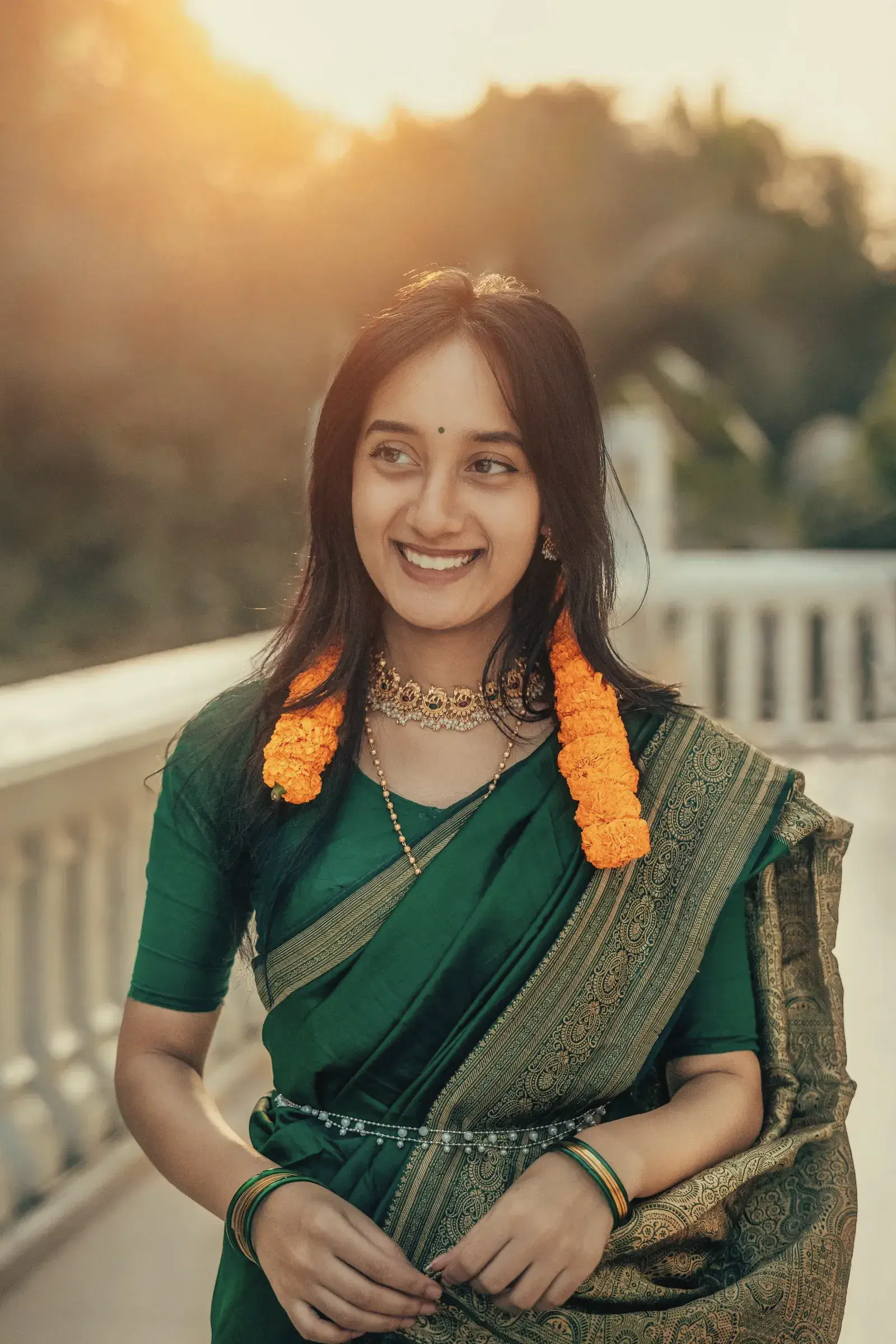 A smiling woman in a peacock matka silk saree with marigolds