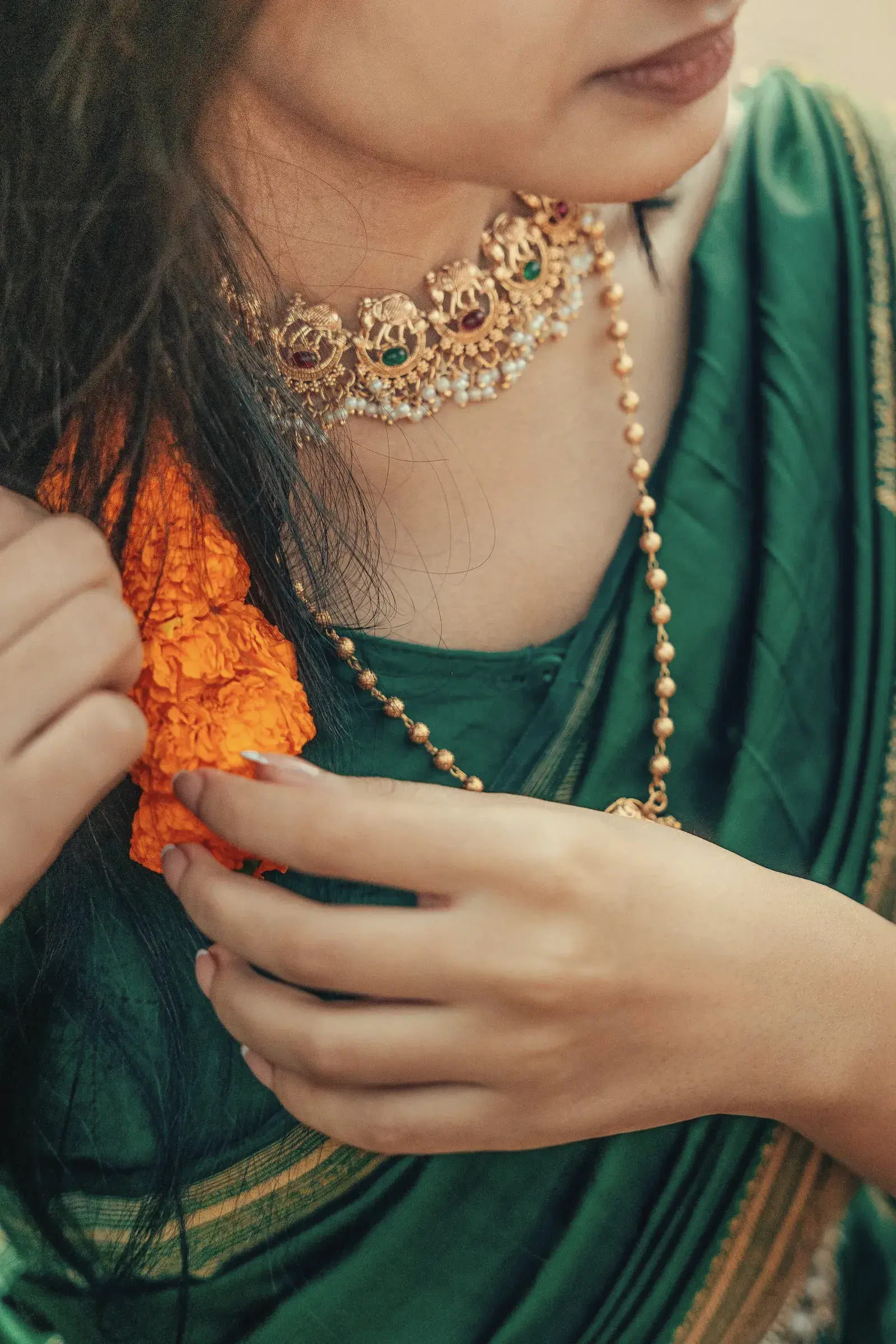 Close view of a peacock matka silk saree with a gold choker and a marigold held at the shoulder