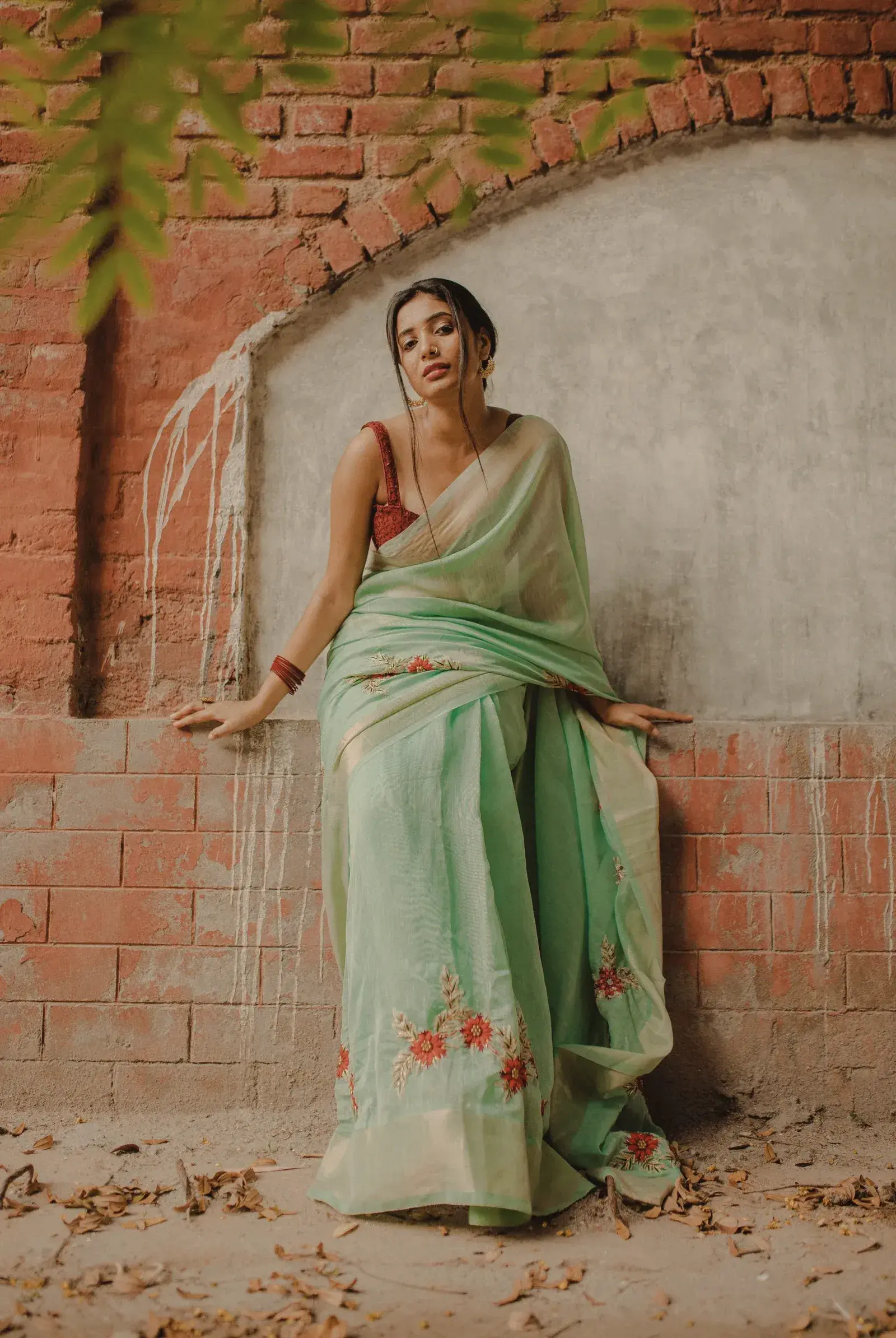 A woman in a mint saree leaning against a weathered brick arch